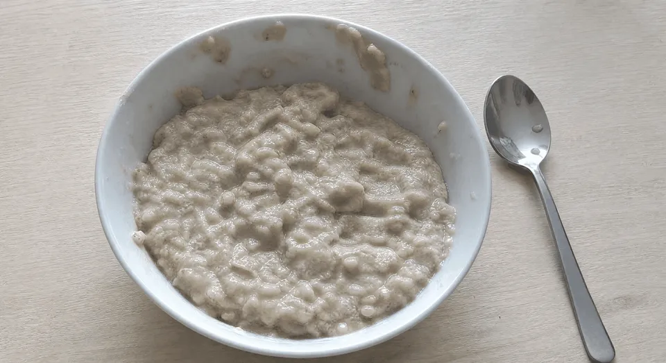 Schüssel mit Haferbrei und Löffel auf hellem Tisch.